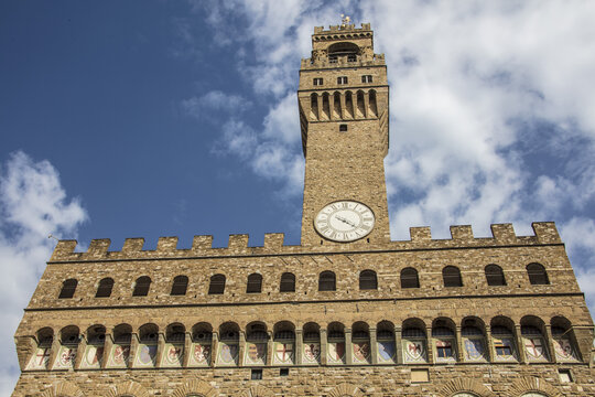 View of the historic Palazzo Vecchio tower with its clock face and stone facade under a blue sky in Florence, Tuscany, Italy.