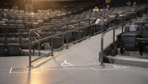 Close view of accessible ramp and seating section in an indoor arena spotlighting inclusive architecture with the rest of the seating softly blurred.