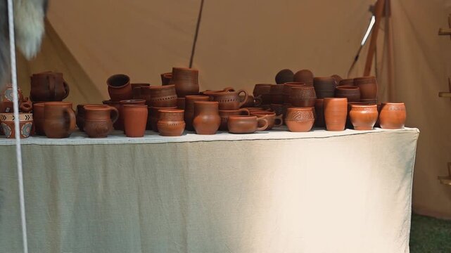 A table shows various pottery items in multiple shapes and sizes. This display takes place at an outdoor market with natural lighting