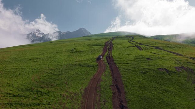 SUV navigating rugged mountain terrain with scenic green hills and clouds