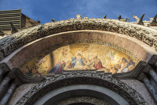 View of the intricate golden mosaic and ornate stone carvings on the facade of St. Mark's Basilica under a clear blue sky in Venice, Veneto, Italy.