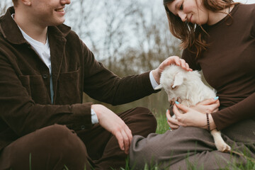 Obraz premium Couple outdoors with a goat kid, gentle interaction, warm atmosphere, lifestyle moment, close-up of care and joy, natural light and grassy backdrop evoke serenity and companionship.