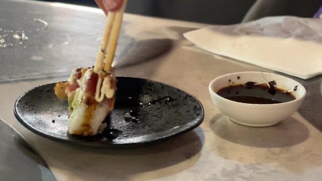 Sushi roll piece held with chopsticks over soy sauce