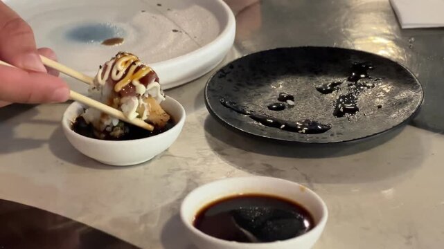 Dipping a sushi roll piece into soy sauce with chopsticks