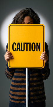 「CAUTION」の黄色い看板を掲げる人物、トラブル防止や警告の概念