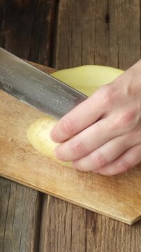 Vertical video. Female hands slicing potato on cutting board. Preparing food.