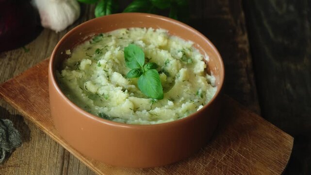 Bowl of mashed potatoes garnished with fresh herbs on rustic wooden table. Thanksgiving meal.