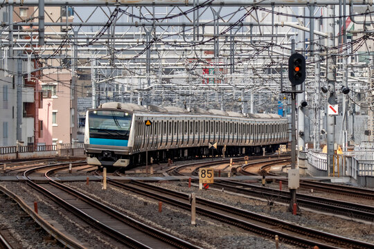 View of a commuter train arriving at Akihabara Station with overhead power lines and urban infrastructure in Chiyoda City, Tokyo, Japan.