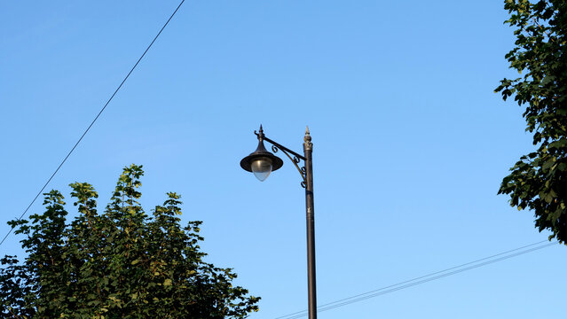 Street lamp, streetlight, pole, lantern, vintage style street light post against blue sky and green trees