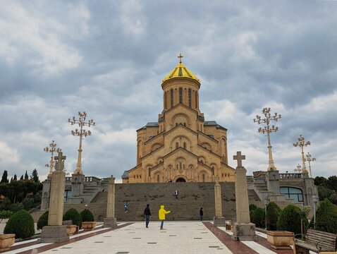 View of the Holy Trinity Cathedral of Tbilisi with its golden dome, stone facade, and grand staircase under a cloudy sky in Tbilisi, Tbilisi, Georgia.