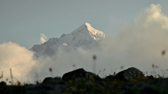 Snow-capped mountain peak emerges from clouds, surrounded by rocky terrain