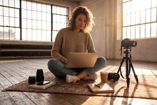 Creadora de contenido freelance editando video con laptop rodeada de equipo fotogr&aacute;fico