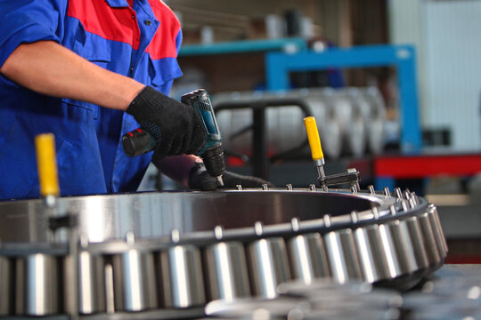 Assembly of a large-sized bearing. Close-up of the industrial bearing assembly process at the factory. A cordless screwdriver in the worker's hand. Heavy industry concept