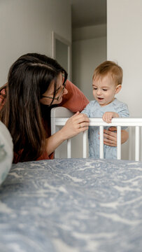 Mother playing with 9 month baby standing in crib at home