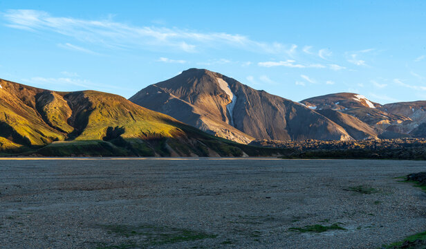 View of the rugged, colorful rhyolite mountains of Landmannalaugar with patches of snow and golden sunlight illuminating the slopes in Iceland.