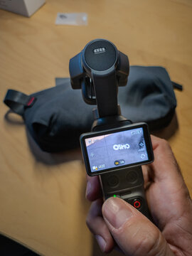 Barcelona, Spain. August 03, 2026, Hand holding the DJI Osmo Pocket 3 camera, showing its screen and controls, with a carry bag in the background