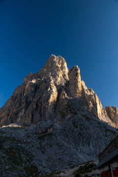 View of the jagged Dolomite mountain peaks illuminated by golden sunlight against a deep blue sky in San Martino di Castrozza, Trentino-Alto Adige, Italy.