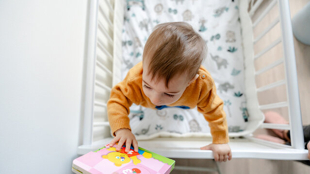 10-month baby climbing in crib reaching colorful toy