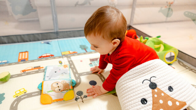 Baby crawling on play mat with toy book at home