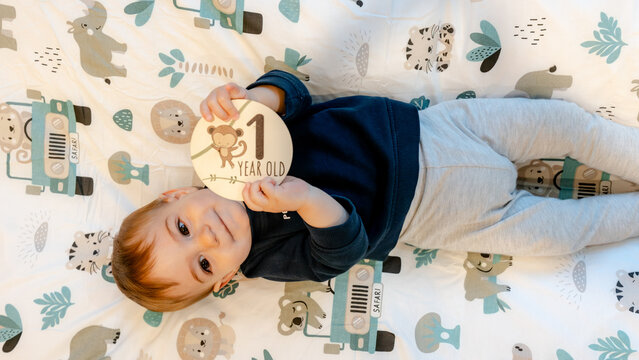 Toddler holding one year old milestone card on baby mat