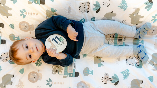 Toddler lying on animal blanket holding 11 month milestone