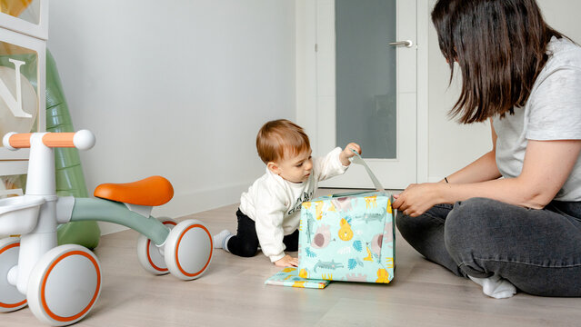 Baby opening birthday gift with parent nearby
