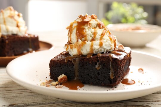 Delicious brownie with vanilla ice cream, caramel sauce and nuts on table, closeup