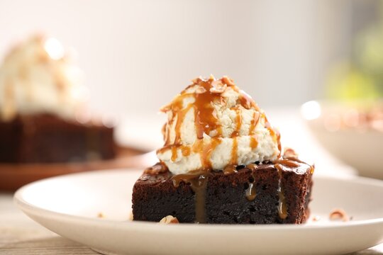 Delicious brownie with vanilla ice cream, caramel sauce and nuts on table, closeup