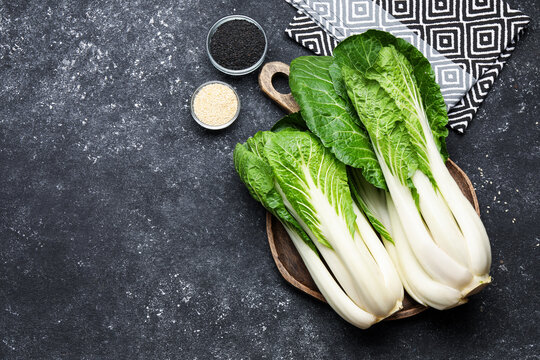 Fresh bok choy cabbages, black and white sesame seeds on gray textured table, flat lay. Space for text