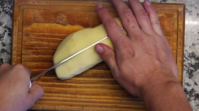 Mano de cocinero cortando papa pelada sobre tabla de madera