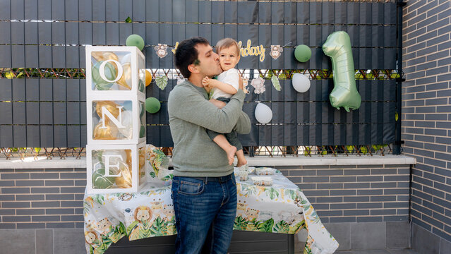 Father kissing baby at outdoor first birthday party