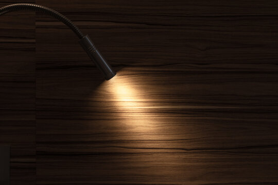 A flexible reading lamp casts a warm, focused glow across a dark wood surface, highlighting grain and creating a cozy, minimalist atmosphere ideal for interiors, product detail, backgrounds