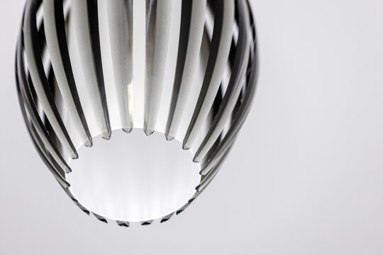 Striped glass pendant light casting soft illumination and subtle reflections in a minimalist monochrome interior. Close-up of geometric pattern, texture and shadow emphasizing contemporary design