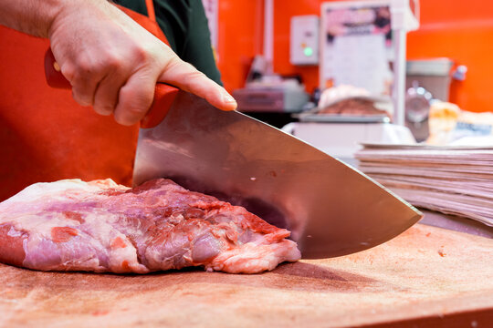 Butcher slicing raw meat with cleaver on cutting board