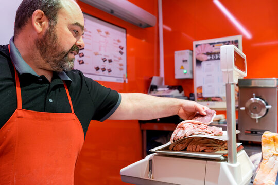 Butcher weighing fresh sliced meat on scale in shop