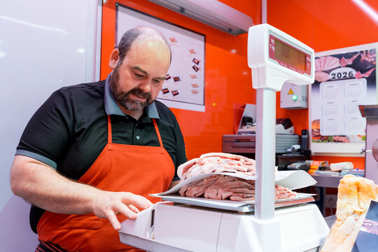 Butcher weighing sliced meat on shop scale for customer