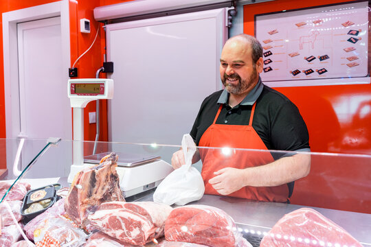 Smiling butcher in apron serving fresh meat at counter