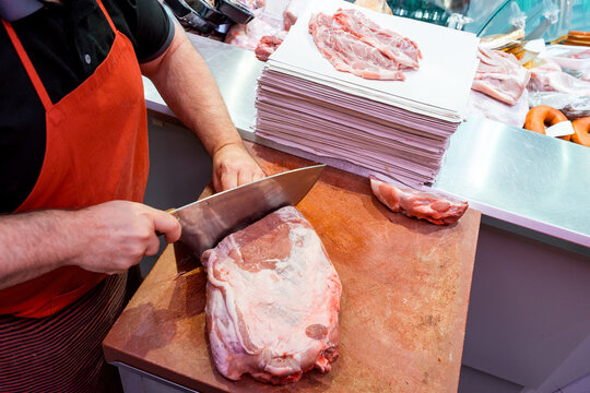 Butcher slicing fresh meat on cutting board in market
