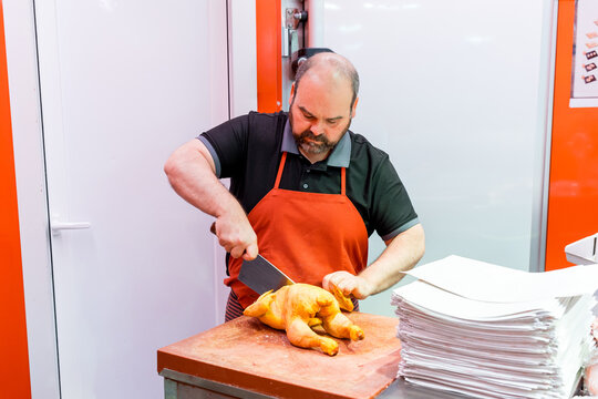Butcher cutting whole chicken on block in meat shop