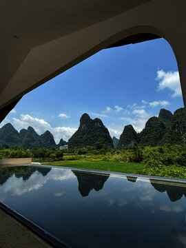 View of the karst mountains of Yangshuo County reflected in a pool with lush green fields under a blue sky in Guilin, Guangxi, China.