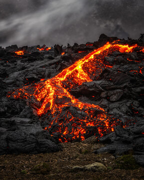 View of a glowing molten lava flow moving over rugged black volcanic rock in Iceland.