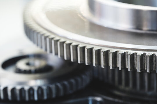 Metallic gears rotate with precision. Sharp teeth reflect light. Polished surfaces show smooth operation. Gray backdrop highlights mechanical detail. Use for engineering projects or machinery topics