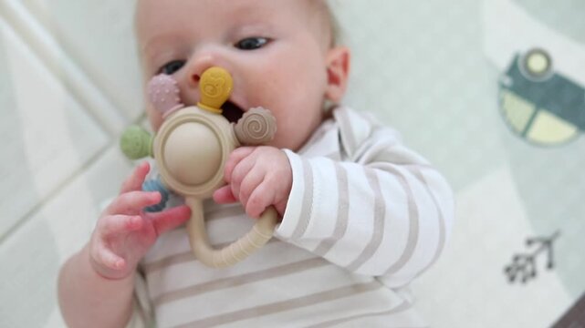 Close-up portrait of a baby chewing a silicone teething toy while lying on a soft blanket, soothing sore gums during teething in a bright nursery setting.