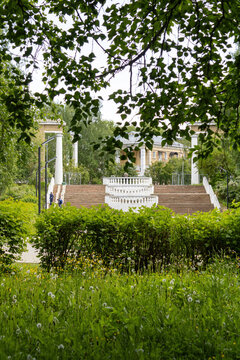 Scenic park with classical stairs and white columns framed by green tree leaves in early summer in the Far North. Lush green northern landscape setting.