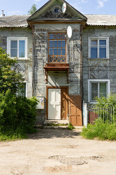Facade of an old weathered wooden residential house with satellite dish in a town in the Far North of Russia. Traditional northern Russian wooden architecture.