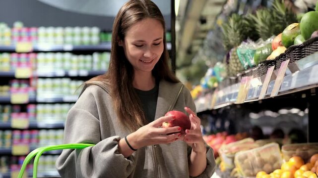 Close-up: a young woman selecting fresh fruit in a supermarket or at a market; a female shopper holding a piece of fresh fruit while shopping.
