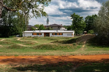 Mini bike pump track in Emmering near Fuerstenfeldbruck, Bavaria, outdoor dirt cycling circuit with clubhouse building and village church tower in green small town landscape © Natalia Schuchardt