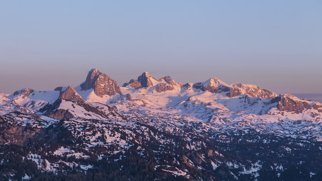 View of the Dachstein glacier peaks illuminated by the golden hour light, with snow-covered slopes and rocky terrain in Liezen District, Styria, Austria.
