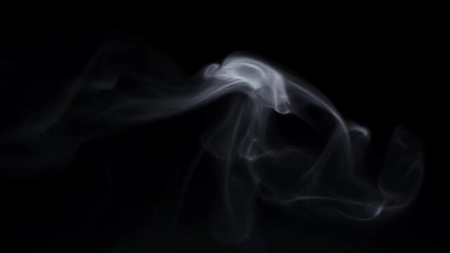 Slow motion static shot of white smoke tendrils swirling and drifting across black background in dark studio environment