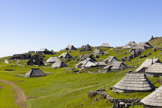 View of traditional wooden shepherd huts with shingle roofs scattered across the green alpine meadows of Velika Planina, Kamnik, Slovenia.